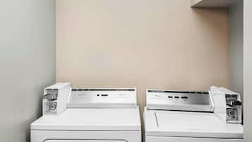 Two white front-loading washing machines in a laundry area with a plain wall and a corner cabinet.
