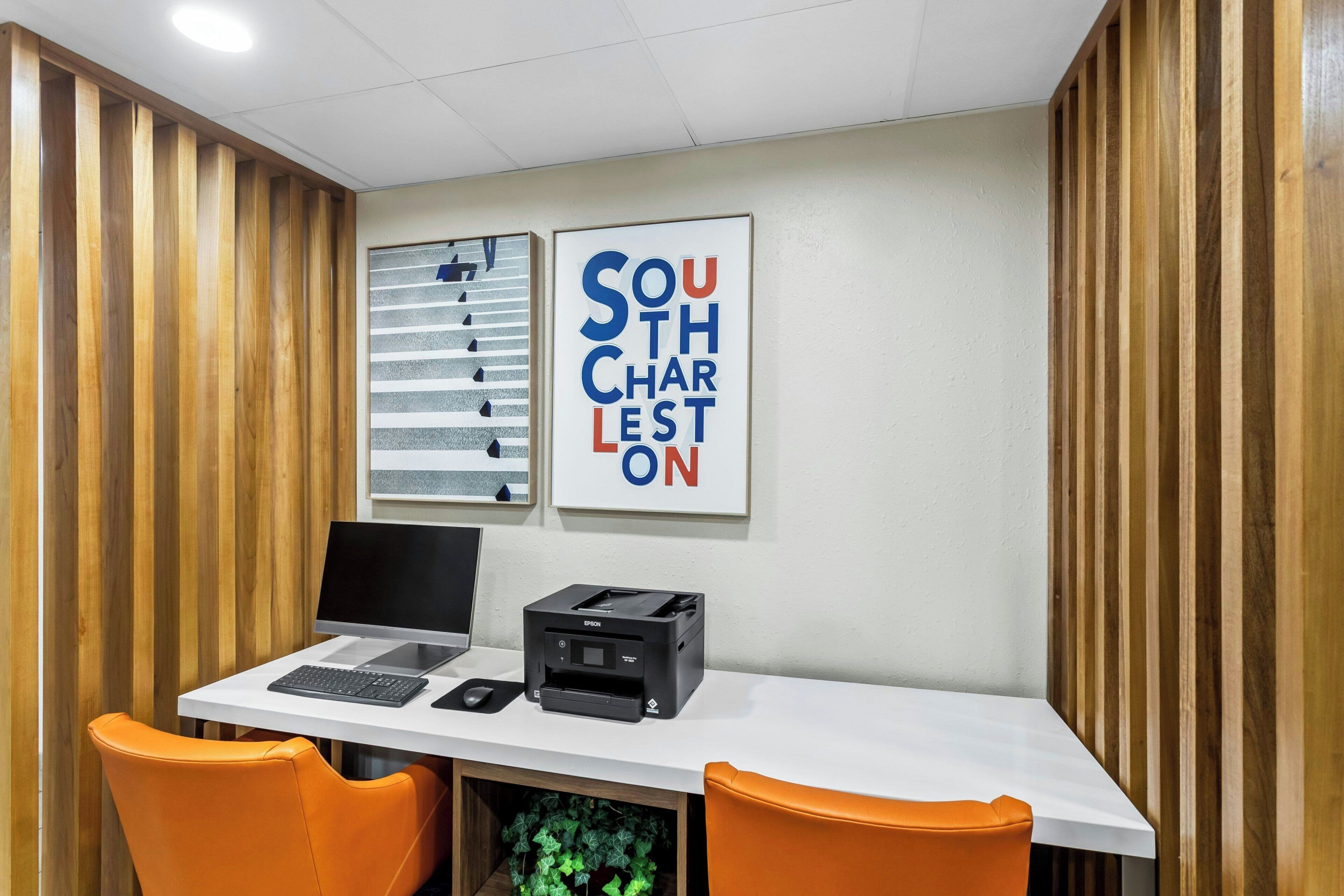 A reception desk with a printer, two laptops, and two orange chairs.