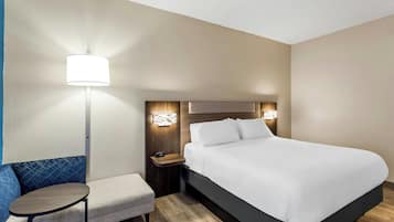 Una habitación de hotel con cama, mesita de noche, lámpara, silla y una pequeña mesa.