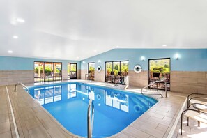 A swimming pool with a tiled floor, surrounded by chairs and tables, and large windows offering views of greenery. - Holiday Inn Express Suites Charleston by IHG (Charleston)