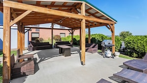 An outdoor patio area with a wooden pergola, seating, and a grill.