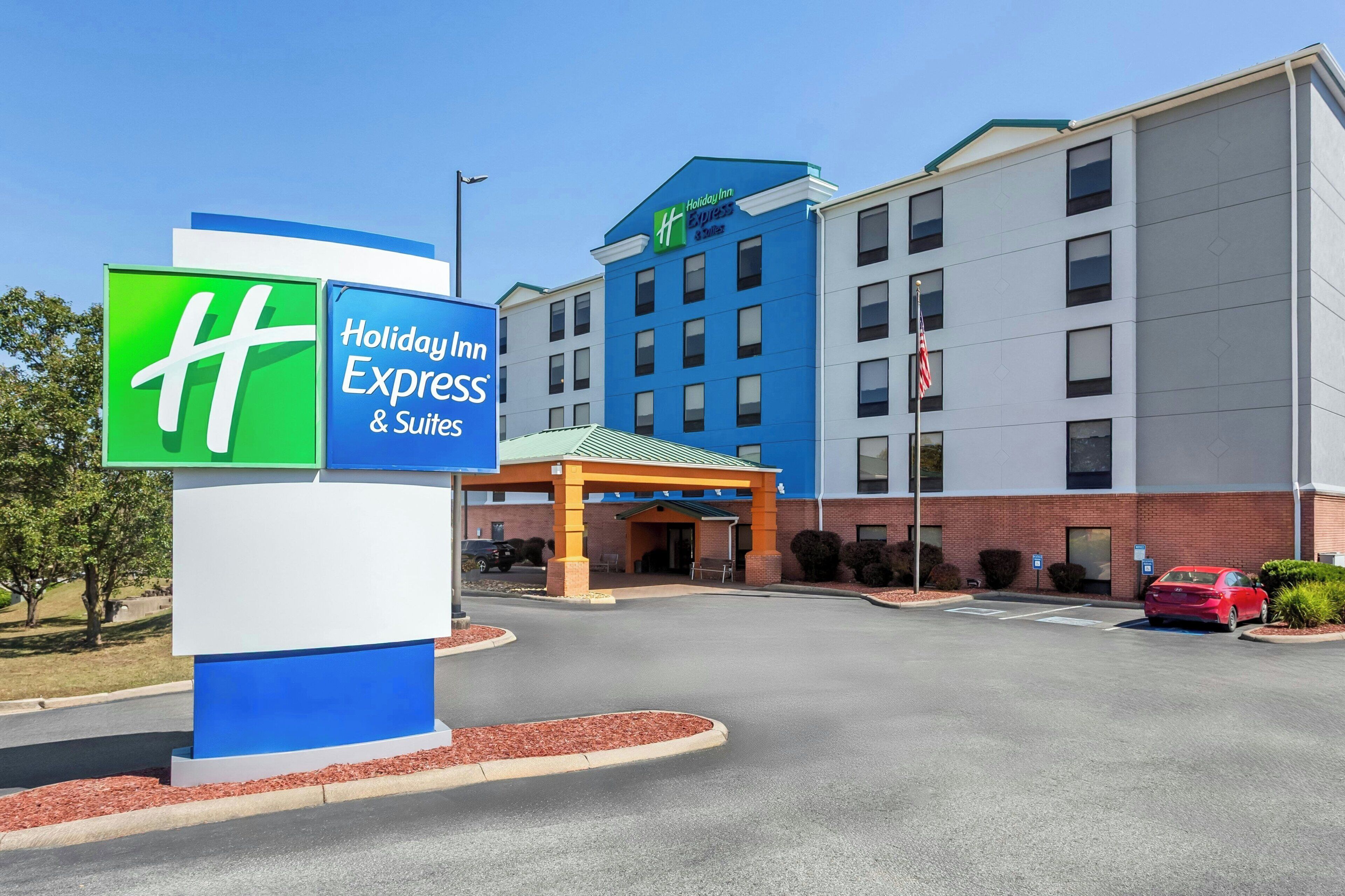 A Holiday Inn Express & Suites building with a clear entrance, parking area, and a sign with the hotel logo.