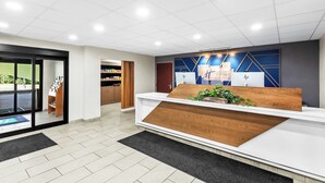 A reception area with a wooden reception desk, a blue wall with geometric patterns, and a glass door entrance.