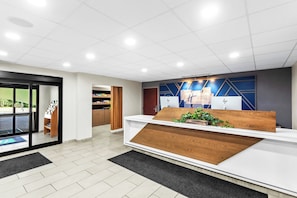 Een receptiegedeelte met een houten receptiebalie, een blauwe muur met geometrische patronen en een glazen toegangsdeur.