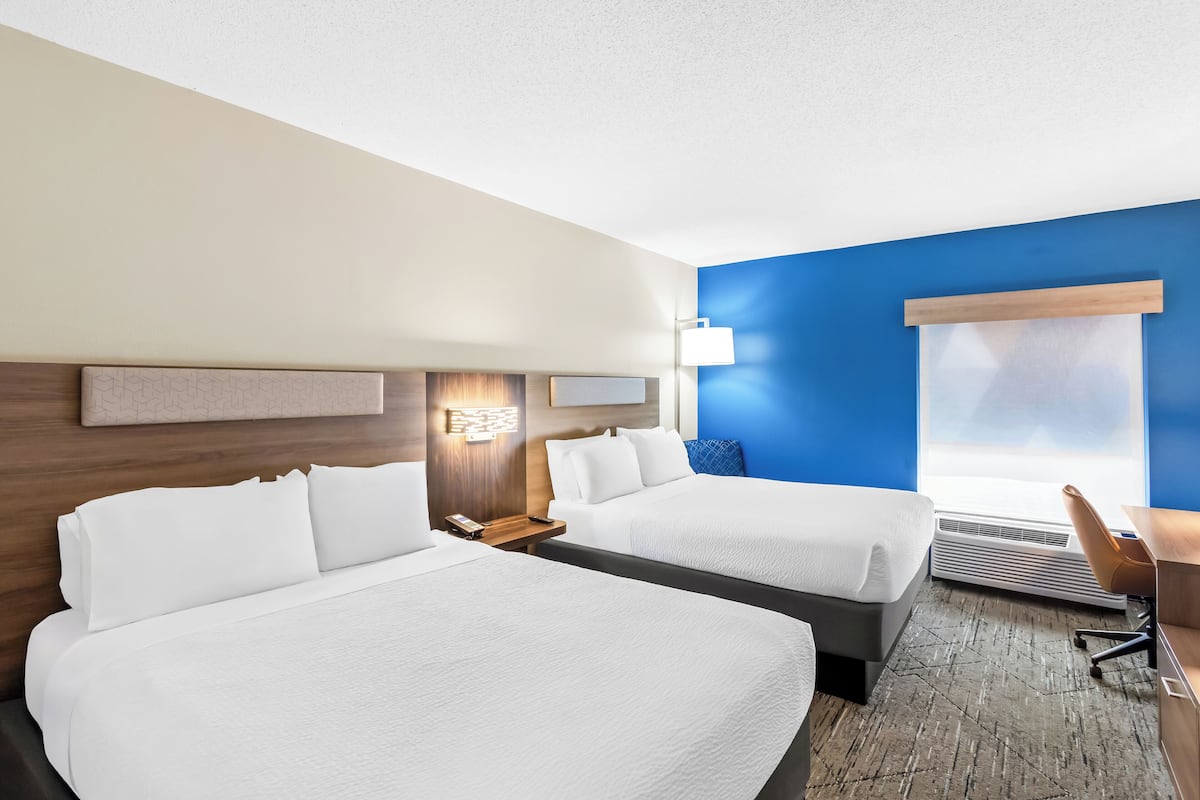Une chambre d’hôtel avec deux lits, un bureau, une chaise, une lampe et une fenêtre.