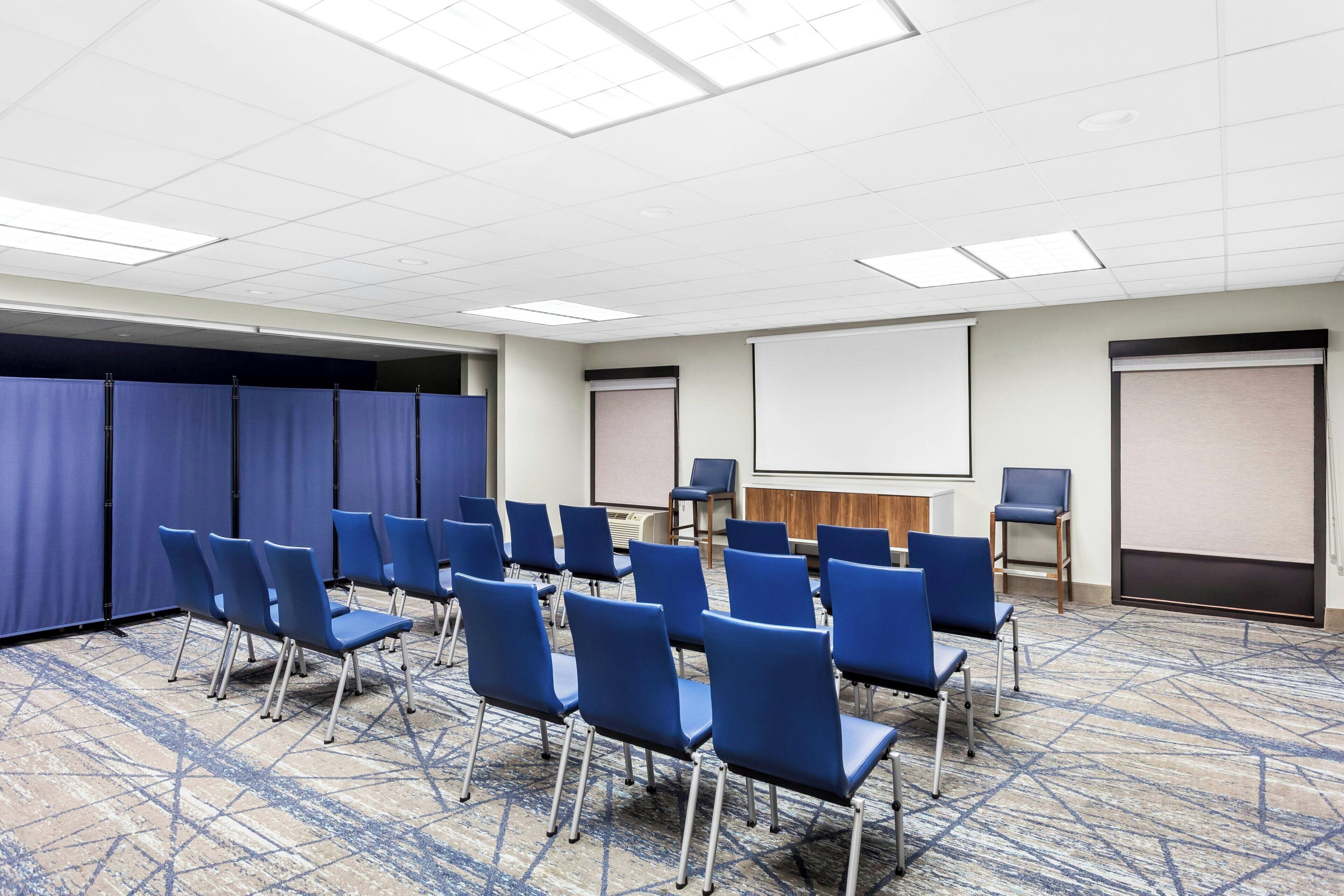 A conference room with rows of blue chairs, a projector screen, and a whiteboard.