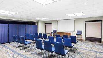 A conference room with rows of blue chairs, a projector screen, and a whiteboard.