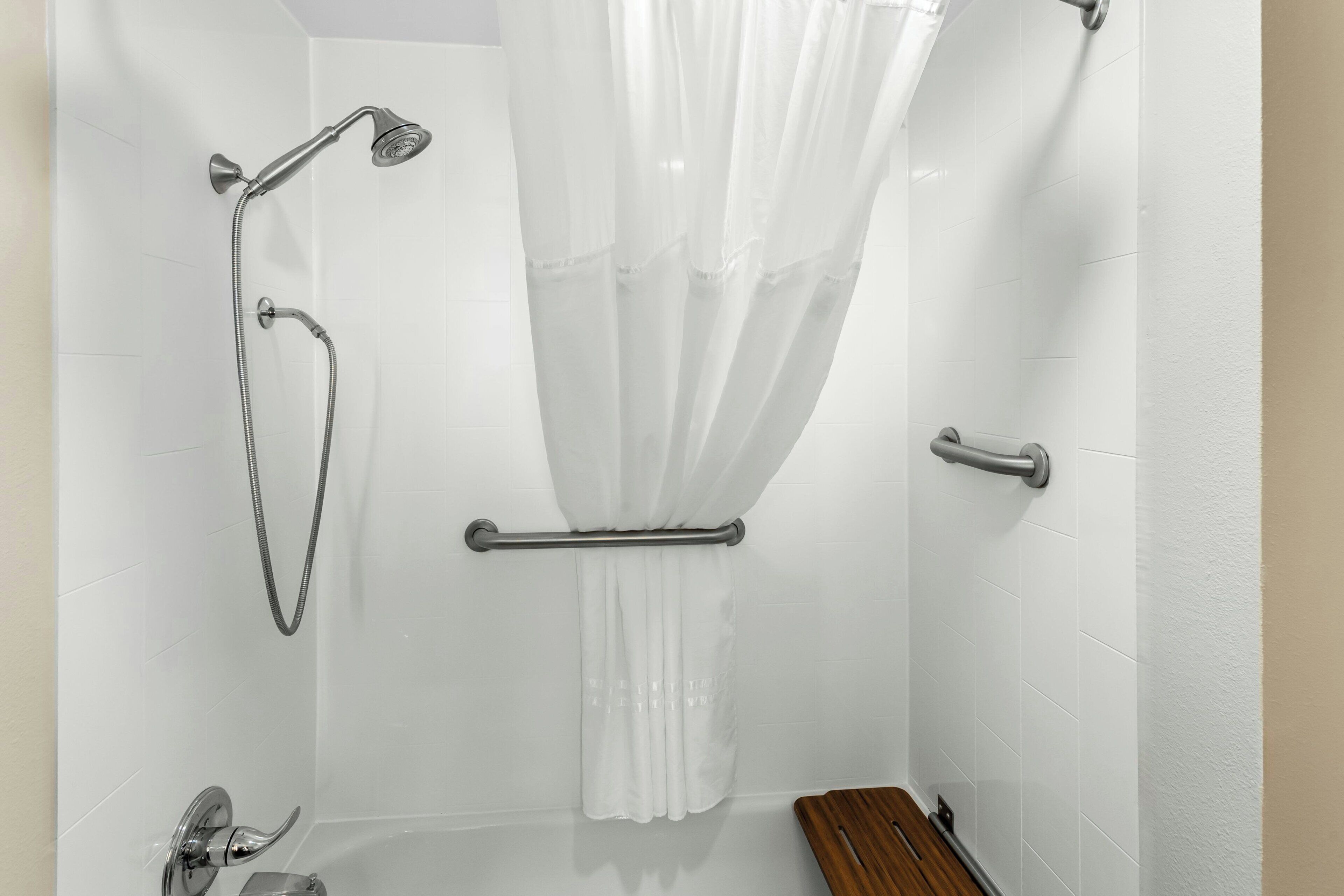 A shower area with a handheld showerhead, a glass-enclosed shower, and a white shower curtain.