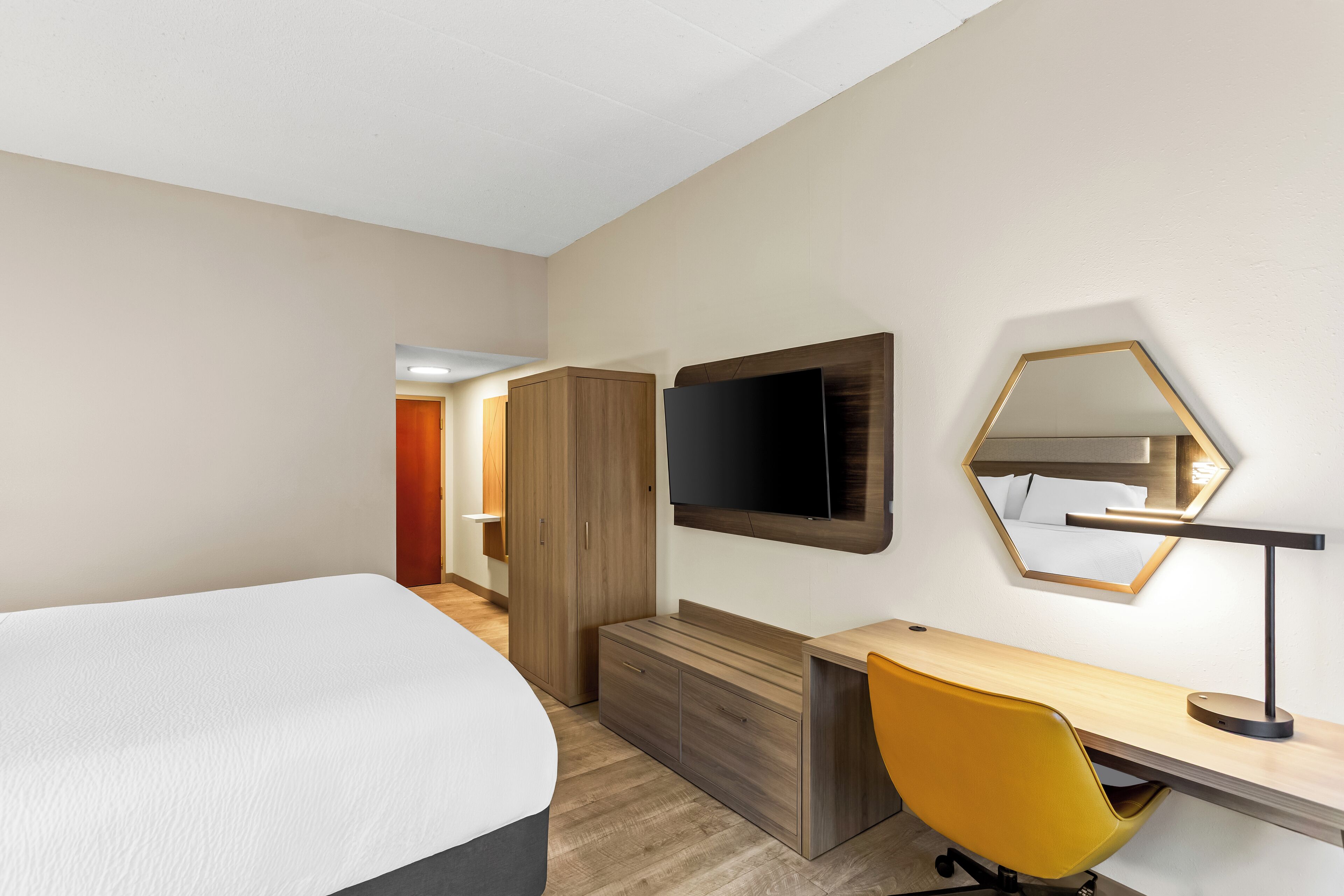 A hotel room with a bed, a desk, a chair, a TV, and a mirror.