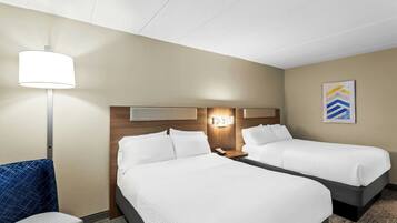 A hotel room with two beds, a desk, a chair, a lamp, and a wall-mounted artwork.