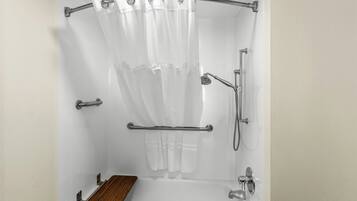 A shower with a white curtain, grab bars, a handheld showerhead, and a wooden bench.