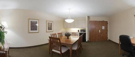 Un comedor amplio con una mesa y sillas de madera, una pequeña cocina con armarios y un microondas, y una puerta que da a otra habitación.