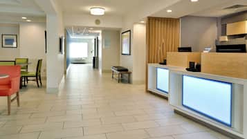 A hotel lobby with a reception desk, seating area, and a hallway leading to other rooms.