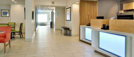 Un vestíbulo de hotel con una recepción, una zona de estar y un pasillo que conduce a otras habitaciones.