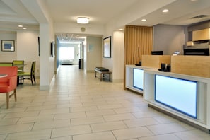 A hotel lobby with a reception desk, seating area, and a hallway leading to other rooms. - Holiday Inn Express Raleigh Durham Airport by IHG (Morrisville)