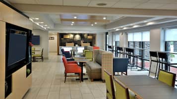 A modern interior with seating areas, a flat-screen TV, and a kitchen in the background.