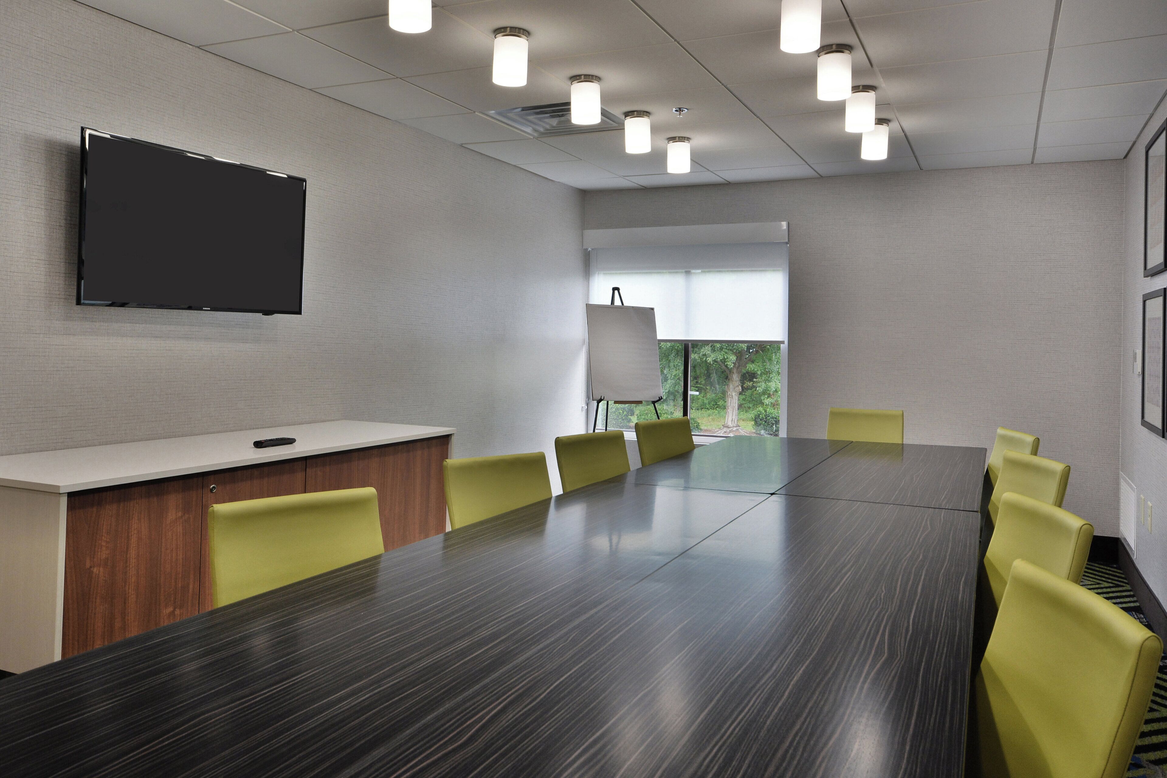A conference room with a long table, yellow chairs, a whiteboard, and a television on the wall.