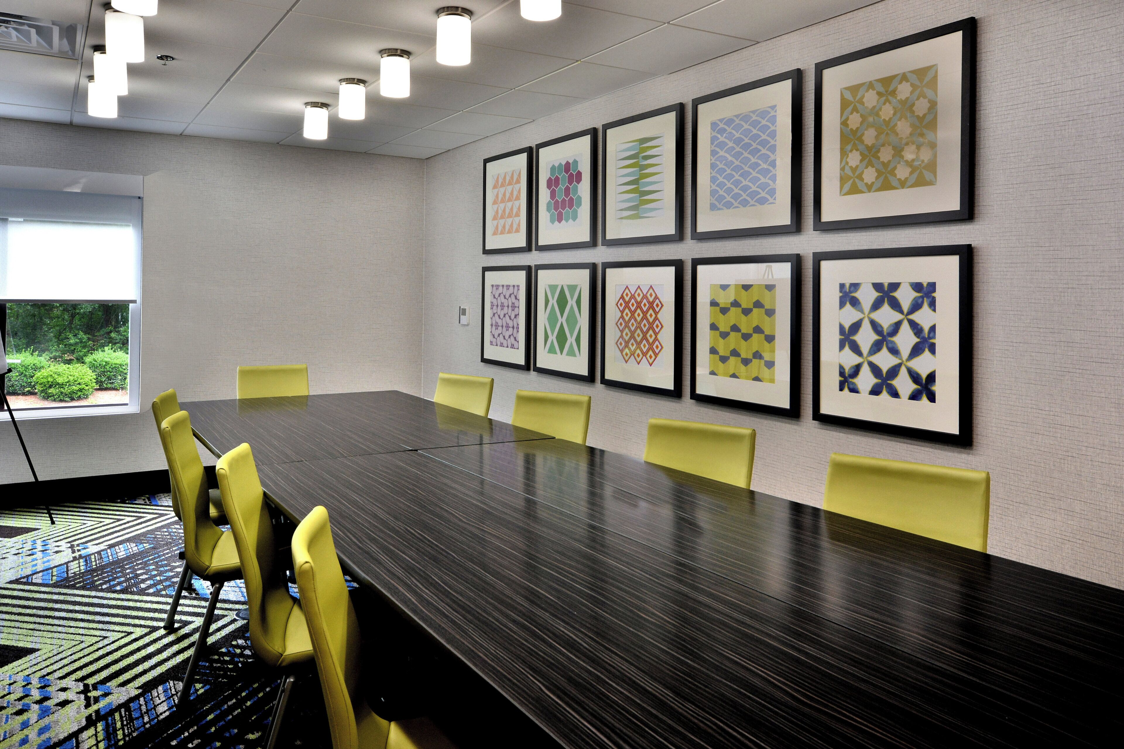 Une salle de conférence avec une longue table, des chaises jaunes et des œuvres d’art encadrées accrochées au mur.