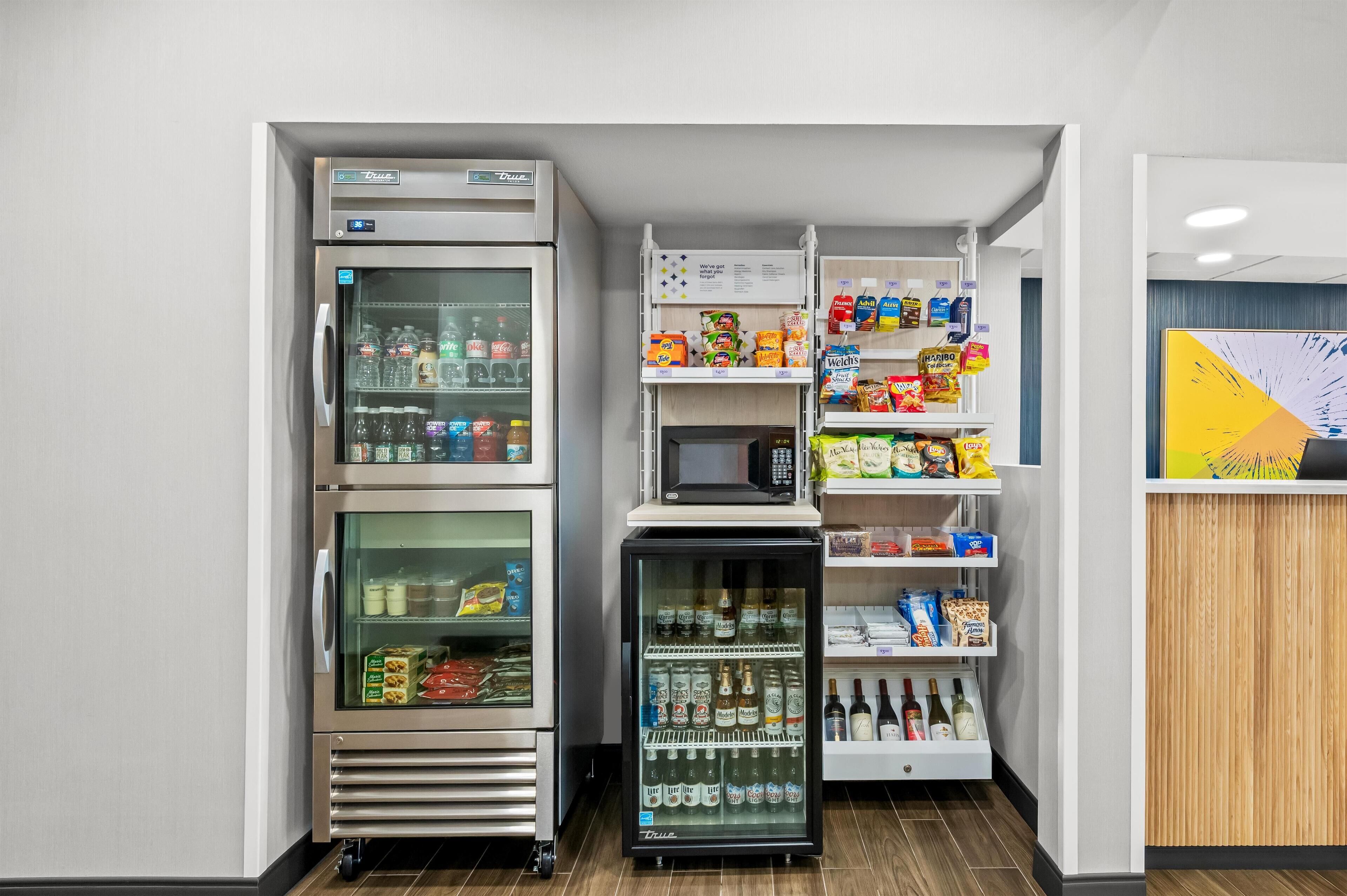 A compact kitchenette with a refrigerator, microwave, and mini-fridge stocked with beverages and snacks.