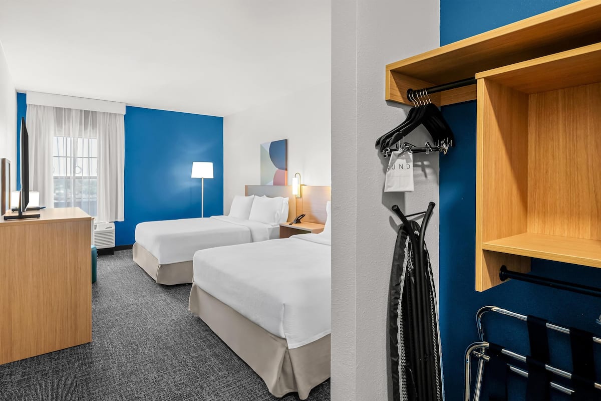 A hotel room with two beds, a desk, a lamp, a wardrobe, and a coat rack.