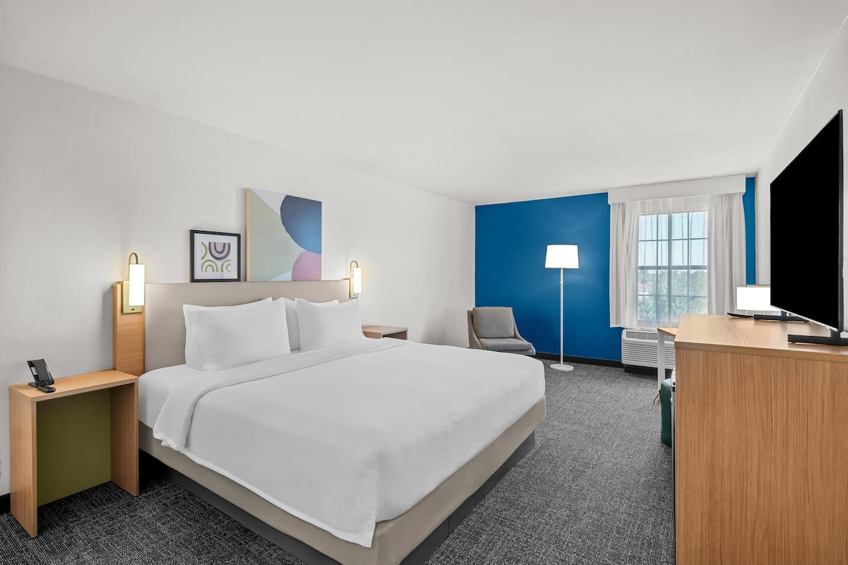 A hotel room with a bed, bedside tables, a desk, a chair, a TV, and a window with curtains.