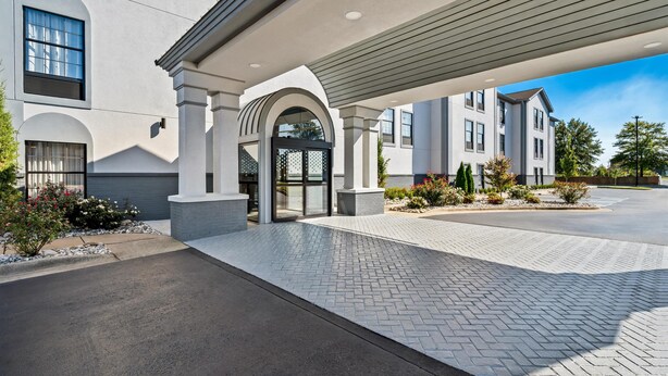 A modern building with a covered entrance, a paved driveway, and landscaped areas with shrubs and flowers. - Spark by Hilton North Little Rock (North Little Rock)