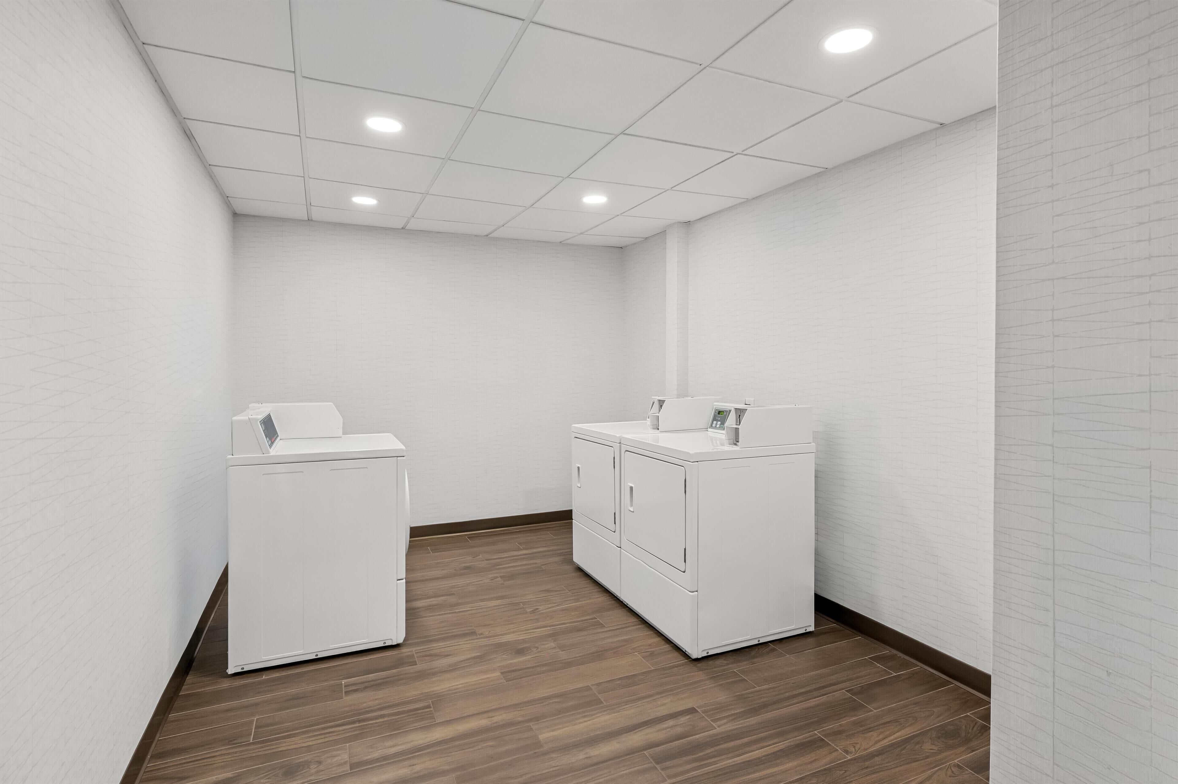 A laundry room with white appliances, wooden flooring, and white brick walls.