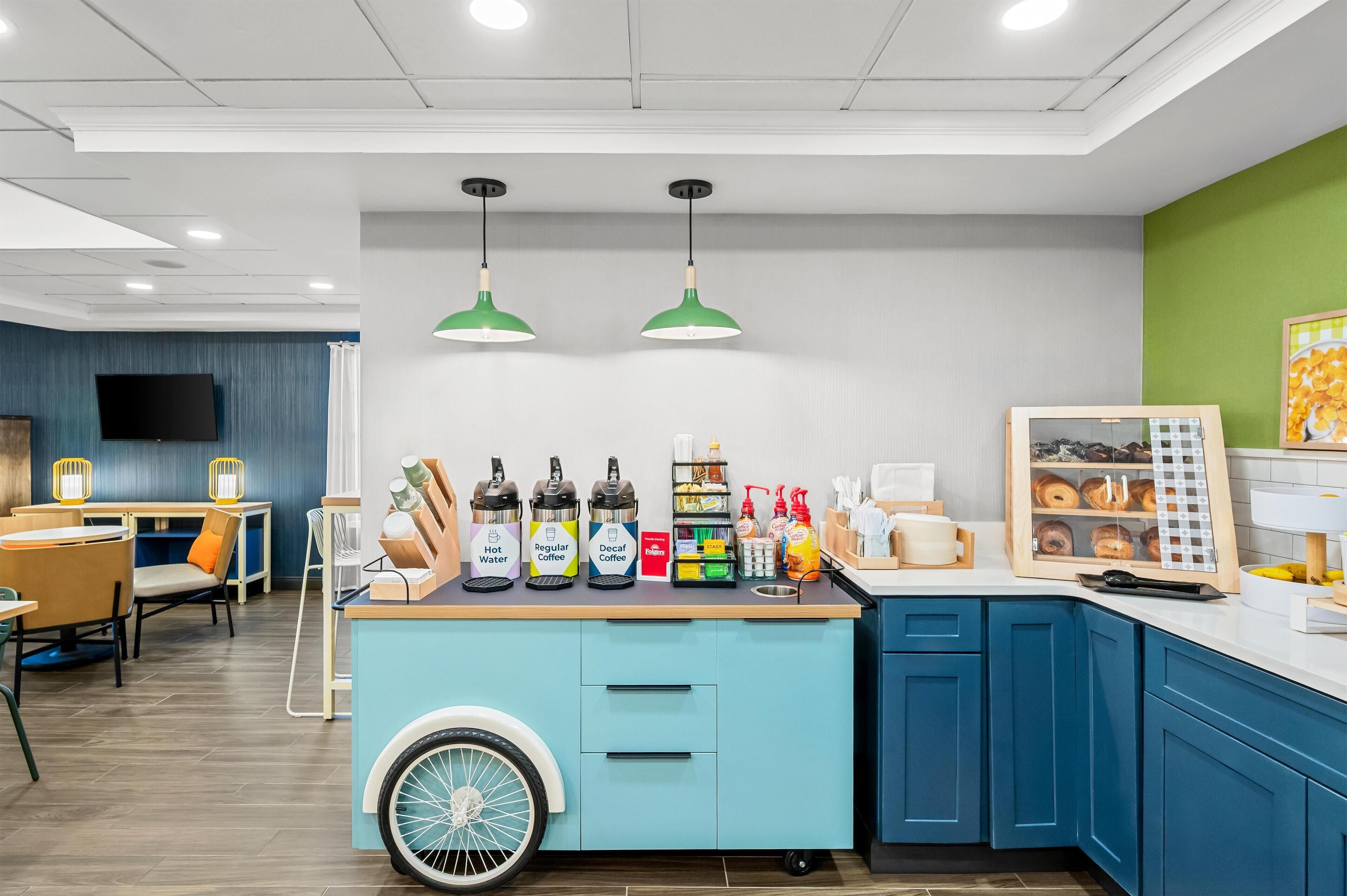 A modern cafe with a blue counter, green pendant lights, and a variety of beverages and snacks.