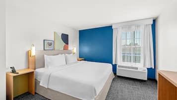 A hotel room with a bed, bedside tables, a window with curtains, and a wall with abstract art.