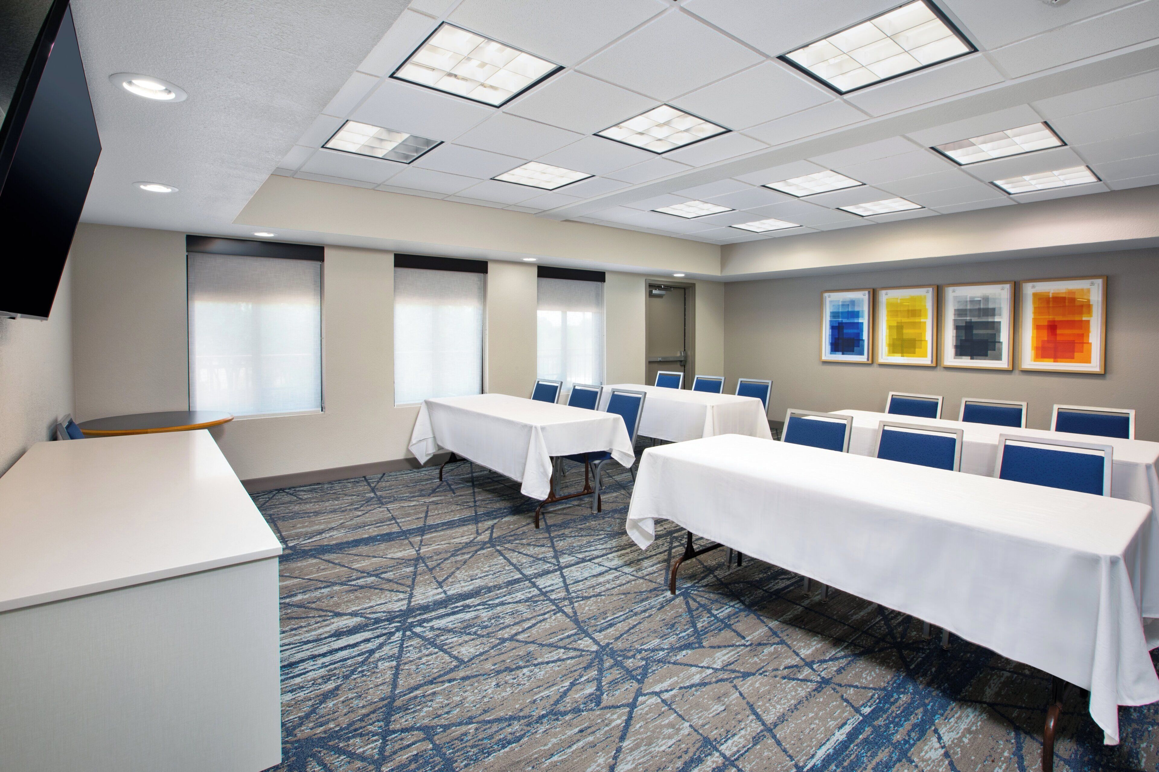 A conference room with tables and chairs, a carpeted floor, and a flat-screen TV mounted on the wall.