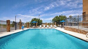 A rectangular swimming pool with a clear blue water surface, surrounded by a stone and metal fence. There are lounge chairs and umbrellas along the poolside. - Holiday Inn Express Silver City by IHG (Silver City)
