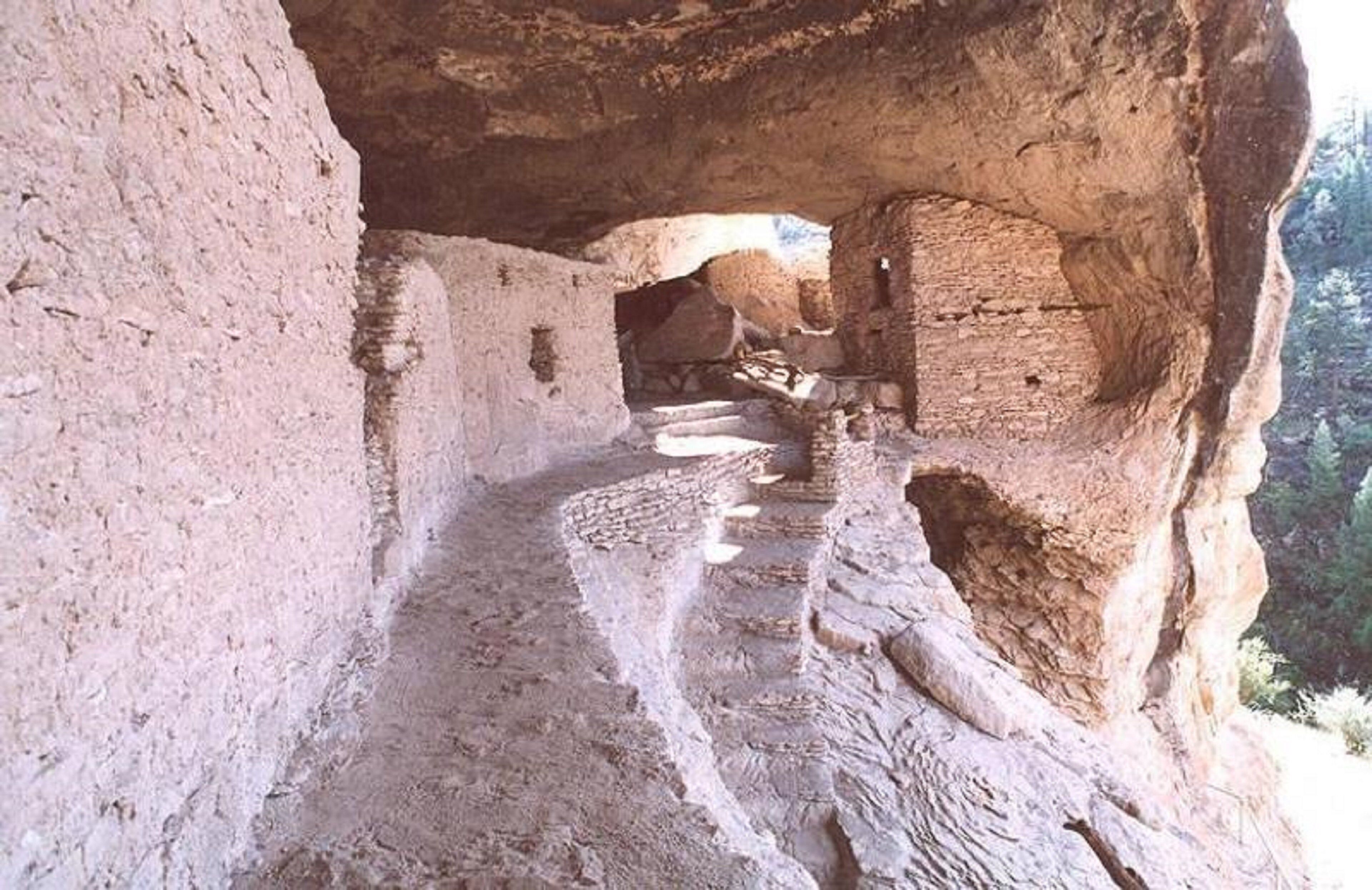 An interior passageway with a stone floor and walls, leading to a natural light source.