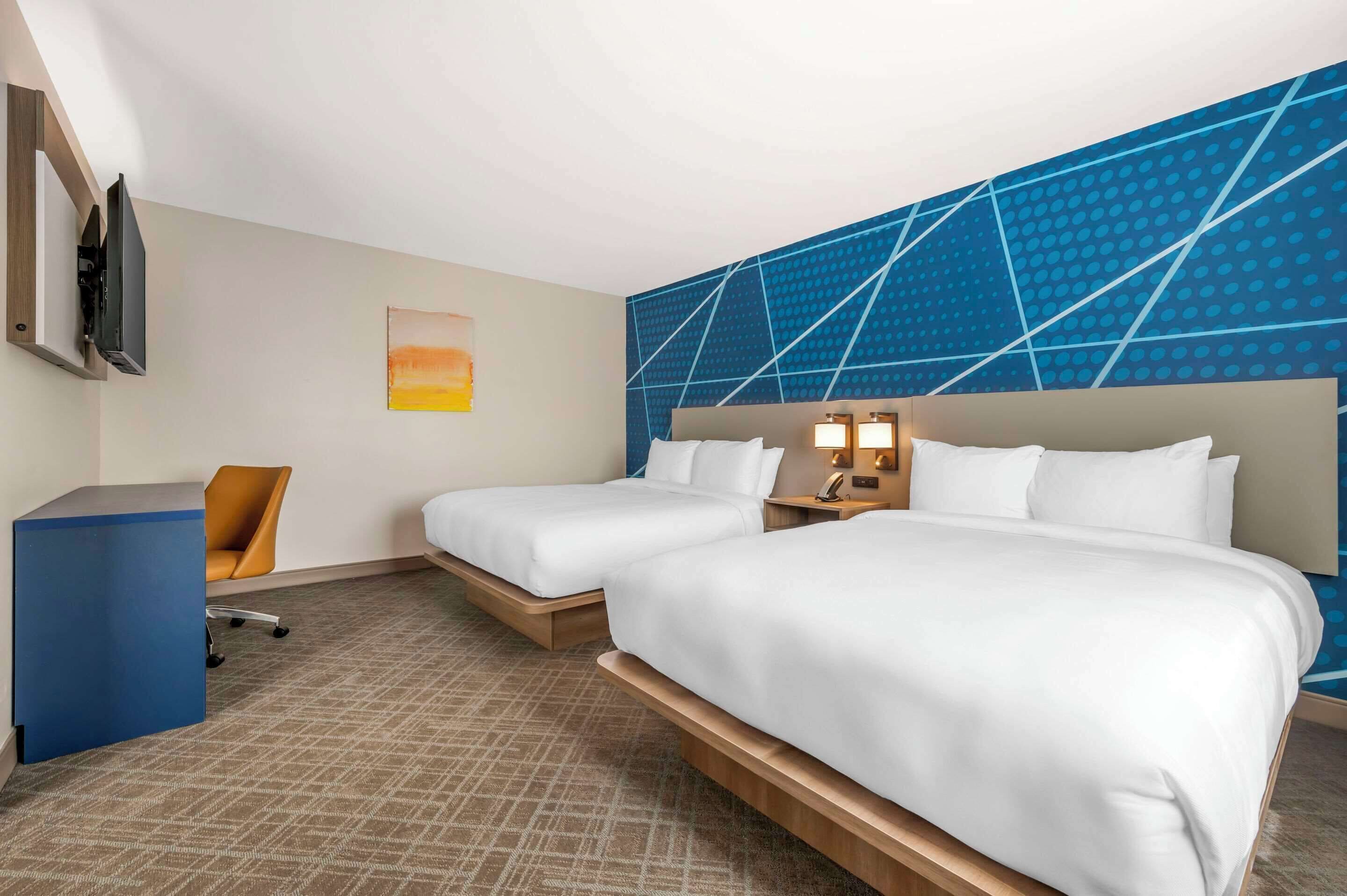 Une chambre d’hôtel avec deux lits, un bureau, une chaise et un téléviseur fixé au mur.
