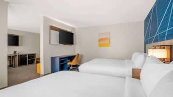 Habitación de hotel con dos camas, un escritorio con silla, televisor y un cuadro en la pared.