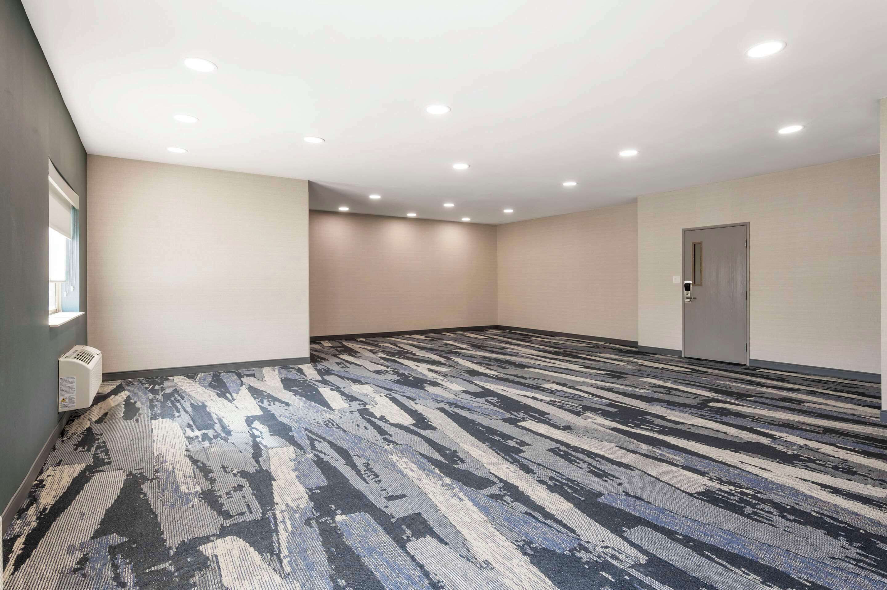 A large, empty conference room with a patterned carpet, recessed ceiling lights, and a door on the right.