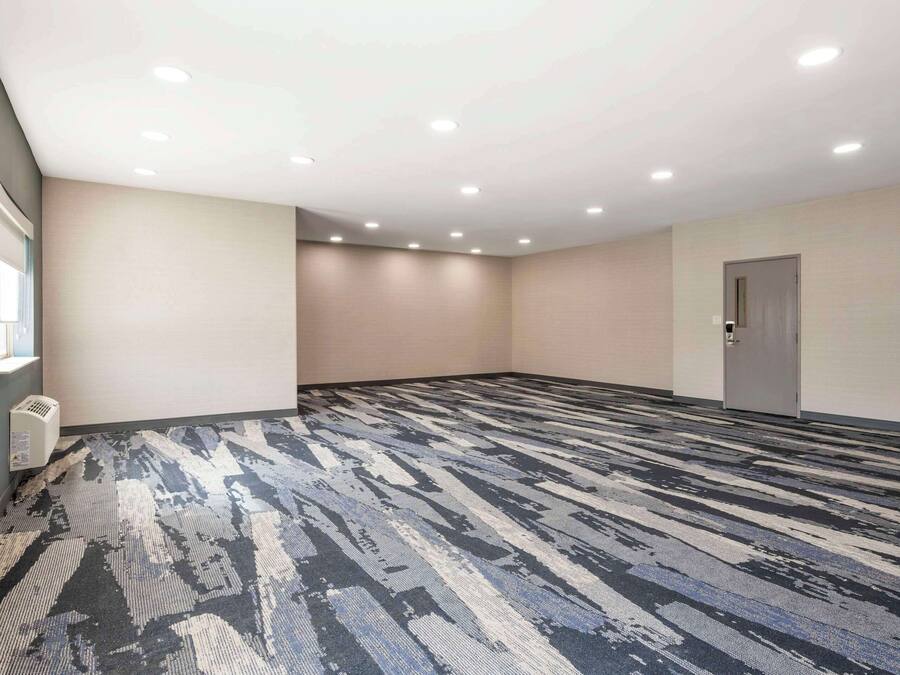 A large, empty conference room with a patterned carpet, recessed ceiling lights, and a door on the right.