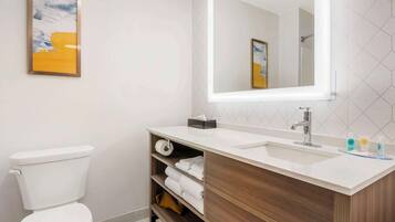 A modern bathroom with a white toilet, a wooden vanity with a sink, and a large mirror.