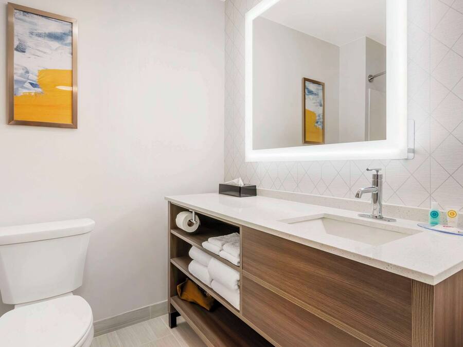 A modern bathroom with a white toilet, a wooden vanity with a sink, and a large mirror.