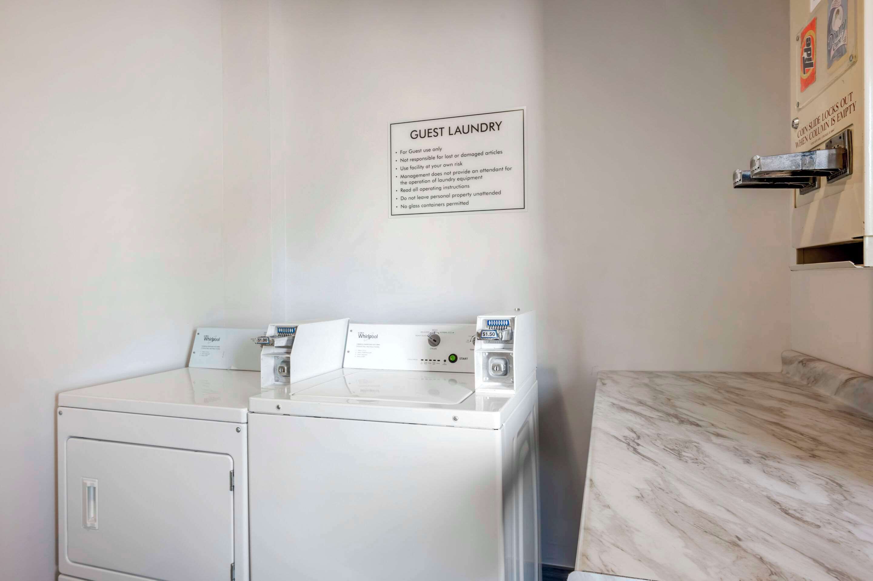 A guest laundry area with two Whirlpool washers and dryers, a sign with laundry instructions, and a marble countertop.