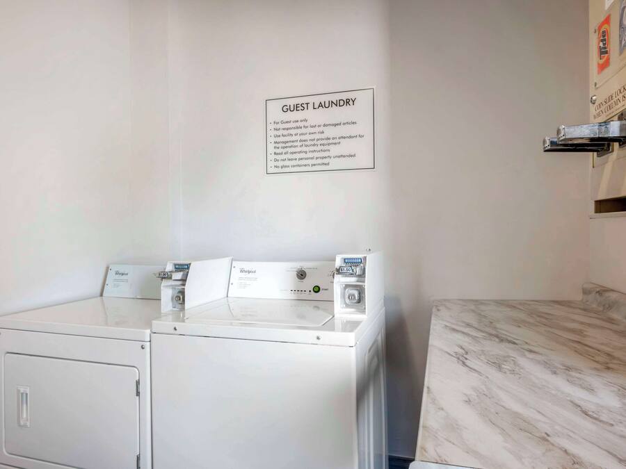 A guest laundry area with two Whirlpool washers and dryers, a sign with laundry instructions, and a marble countertop.
