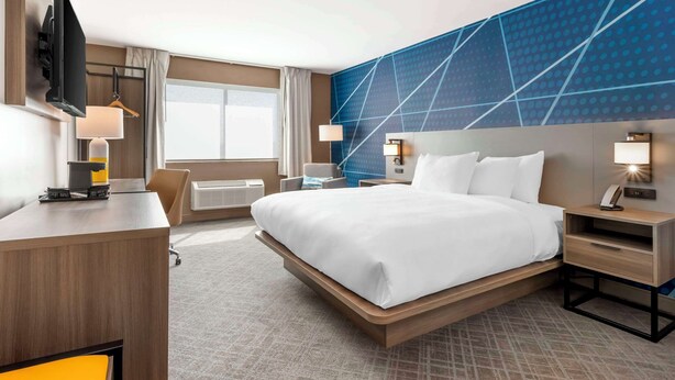 Une chambre d’hôtel avec un grand lit, un bureau, un téléviseur à écran plat et un téléviseur fixé au mur.