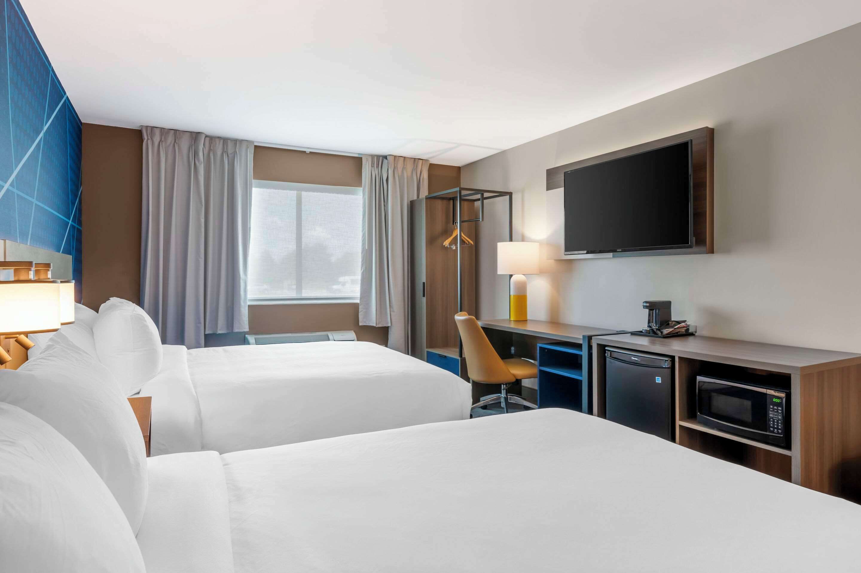 Ein Hotelzimmer mit zwei Betten, einem Schreibtisch mit Computer, einer Mikrowelle und einem Fernseher.