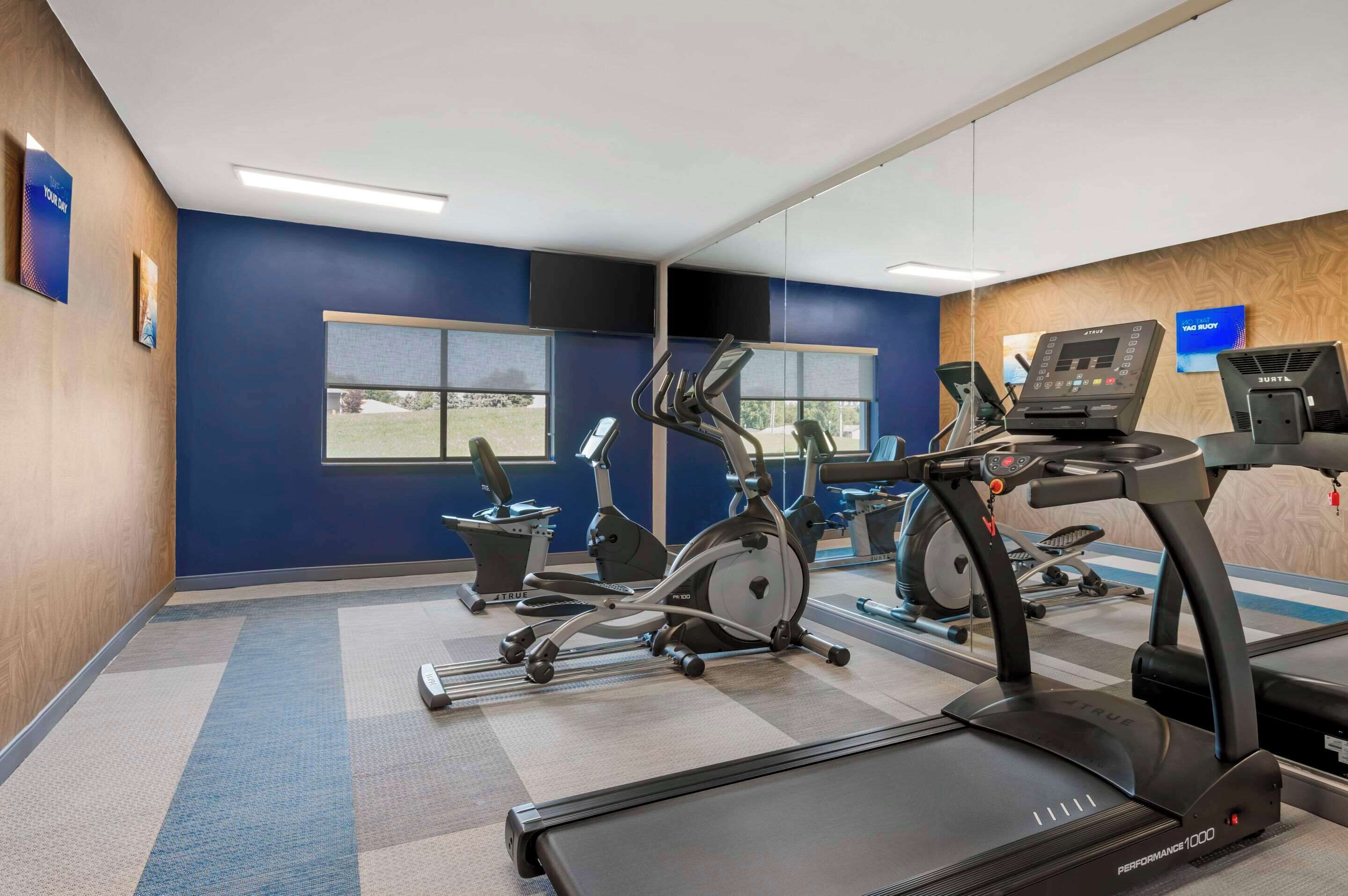 A gym with various exercise equipment, including treadmills and stationary bikes, and large windows providing natural light.