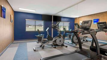 A gym with various exercise equipment, including treadmills and stationary bikes, and large windows providing natural light.