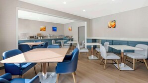 Un espace repas moderne avec des chaises bleues et blanches, des tables blanches et une cuisine en arrière-plan.