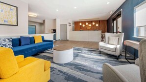 Un salon moderne avec un canapé bleu, un fauteuil jaune et un fauteuil blanc. Une table basse en bois se trouve au centre de la pièce.