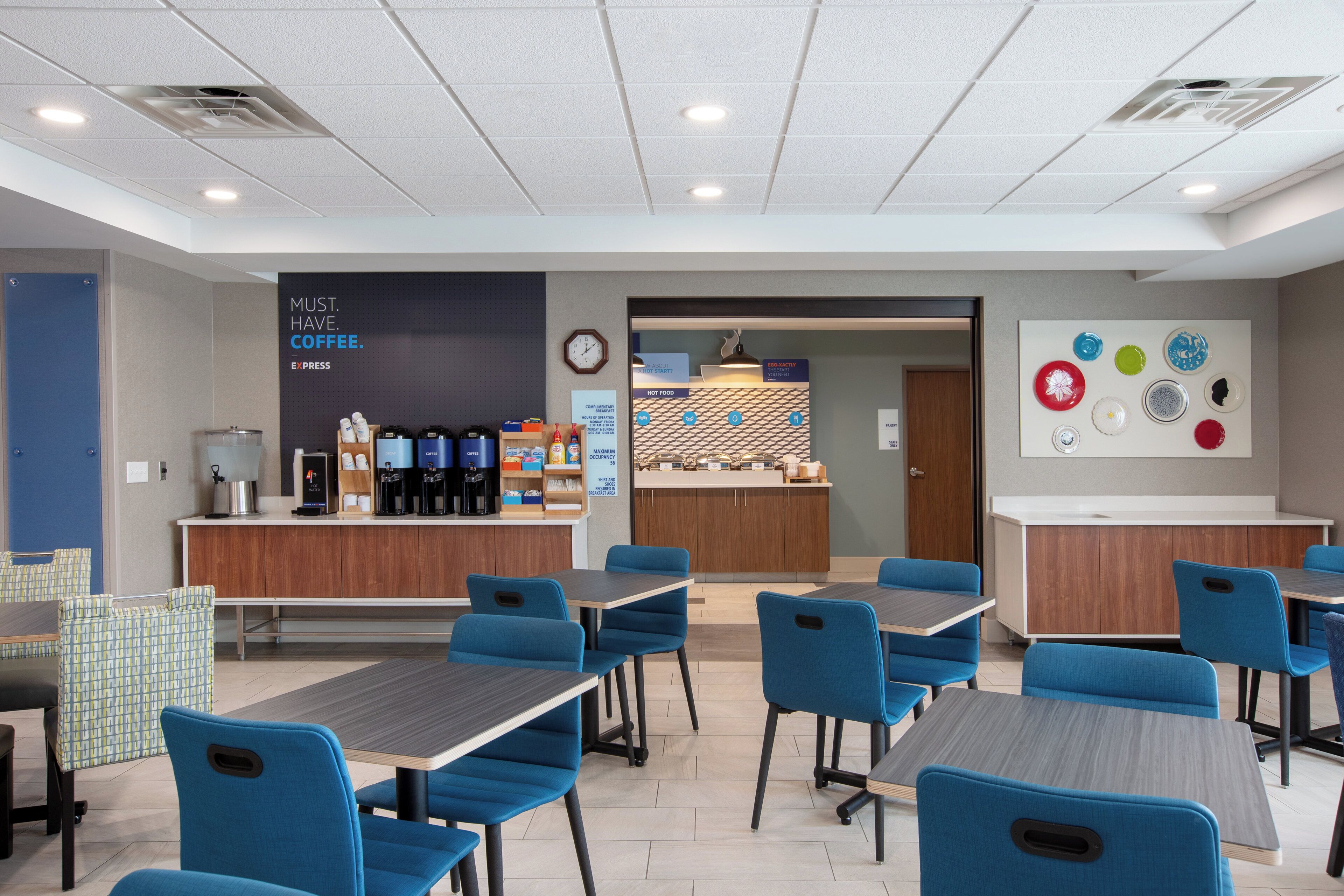 Un café moderno con sillas azules, una estación de café y una pared con un reloj y un letrero.