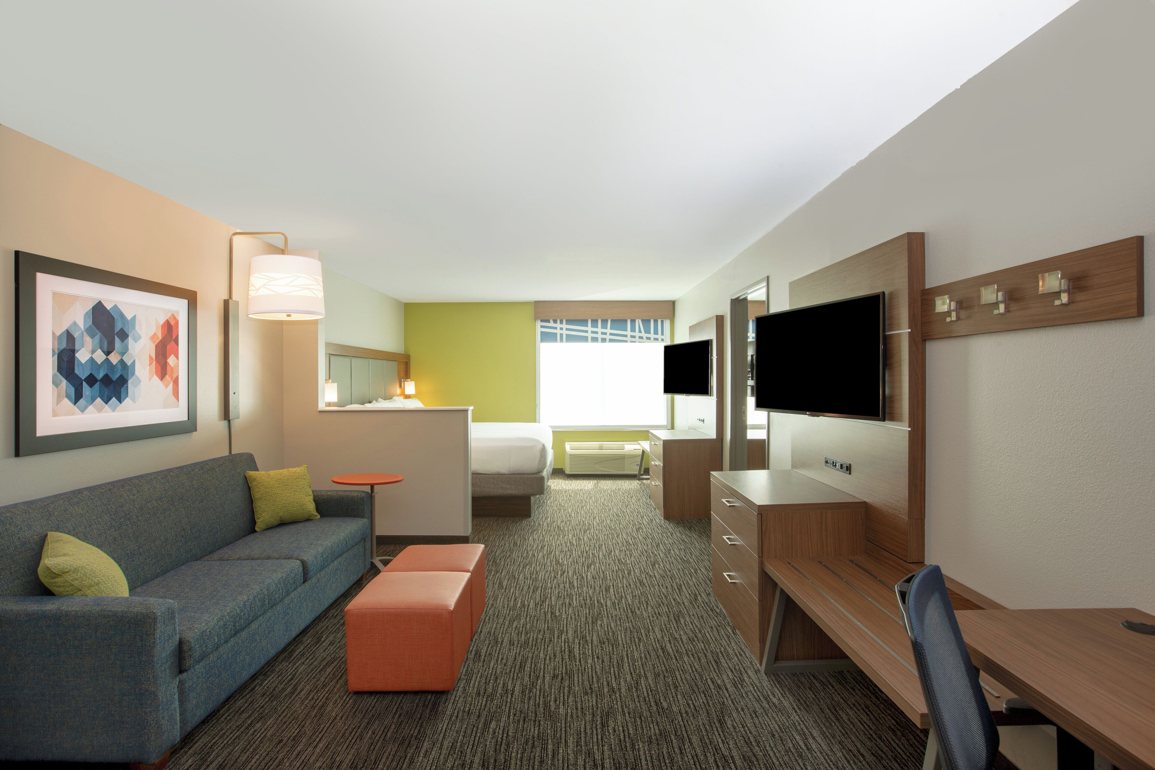 A hotel room with a sofa, a small table, a TV, and a desk.