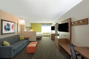 A hotel room with a sofa, a small table, a TV, and a desk.