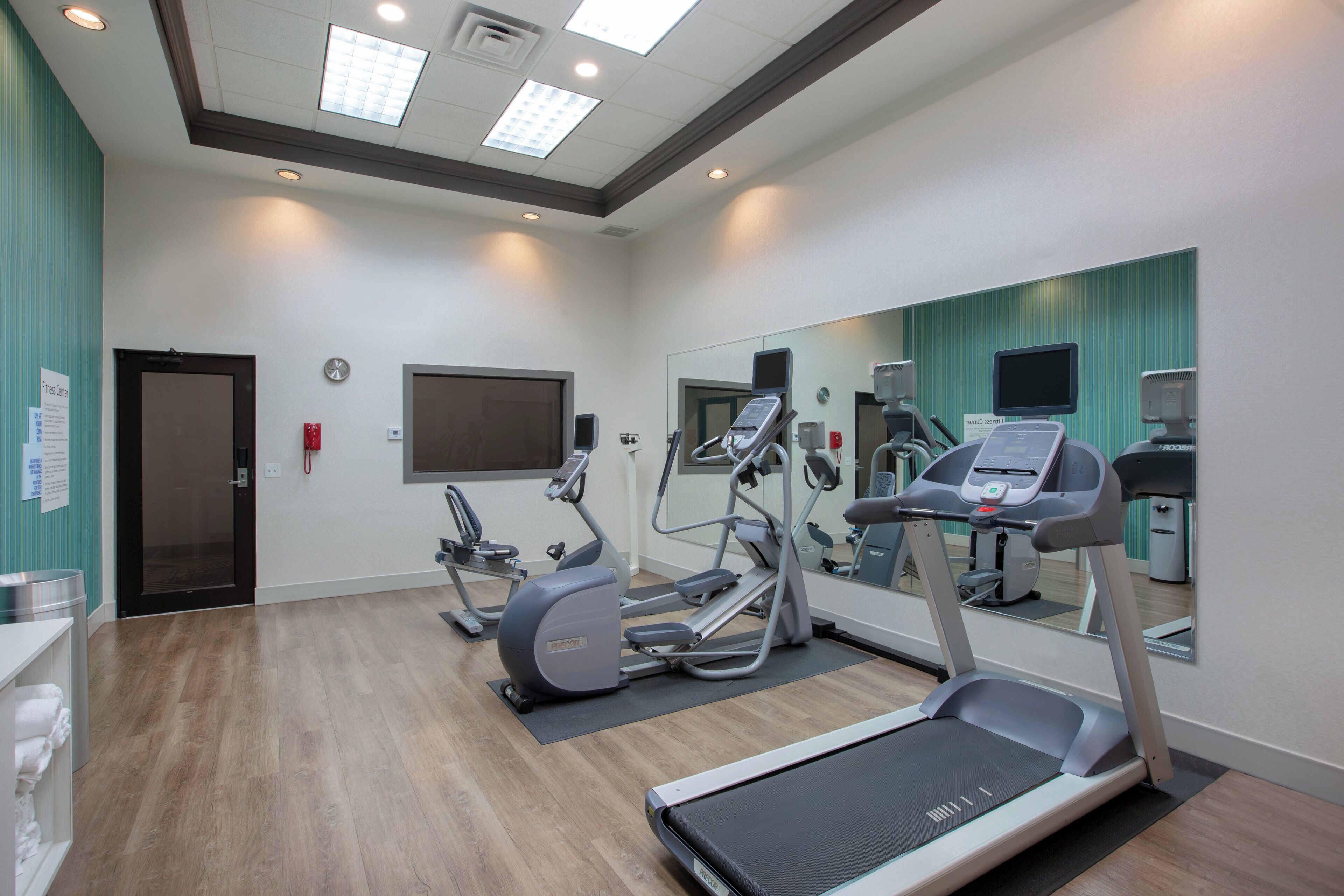 A fitness center with treadmills, elliptical machines, and a mirrored wall.